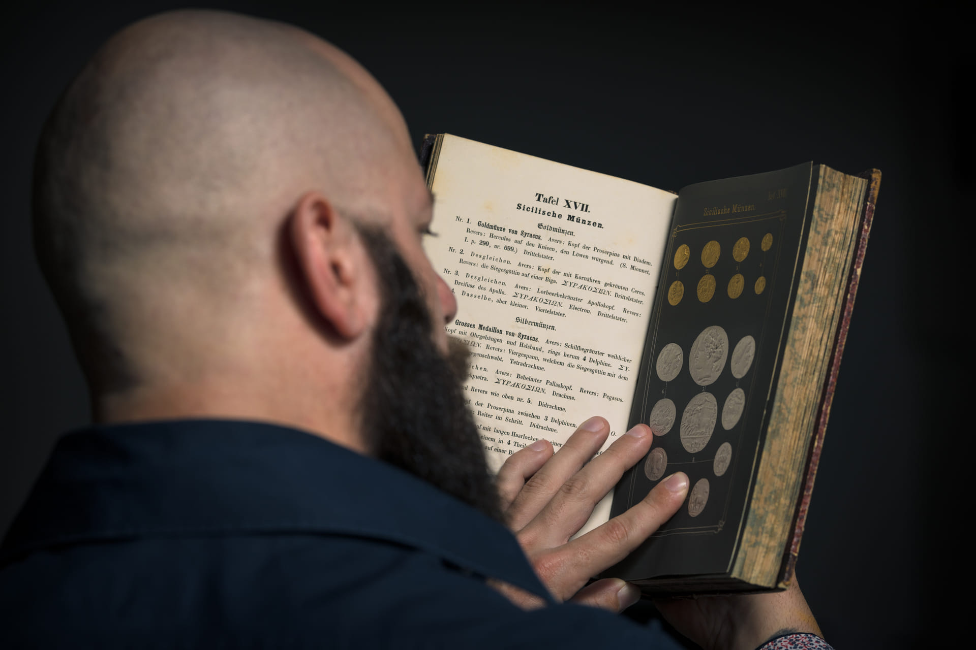 A numismatist studying historical reference literature illustrating ancient coins.